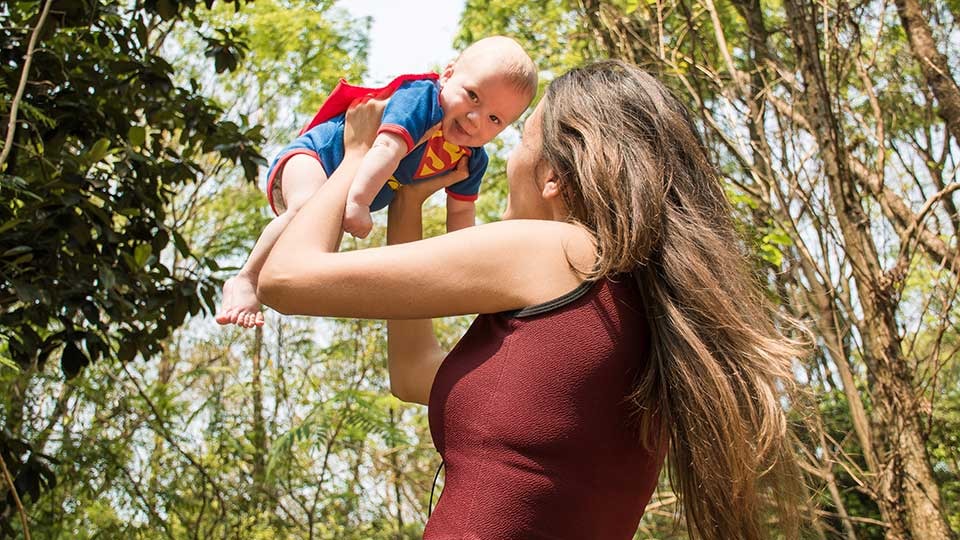 Mutter hält Baby im Superman-Kostüm in die Höhe